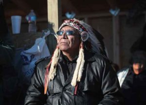 CANNON BALL, ND - DECEMBER 04: Chief Arvol Looking Horse of the Lakota/Dakota/Nakota Nation listens to speakers during an interfaith ceremony at Oceti Sakowin Camp on the edge of the Standing Rock Sioux Reservation on December 4, 2016 outside Cannon Ball, North Dakota. Native Americans and activists from around the country have been gathering at the camp for several months trying to halt the construction of the Dakota Access Pipeline. Today the US Army Corps of Engineers announced that it will not grant an easement for the pipeline to cross under a lake on the Sioux Tribes Standing Rock reservation, ending the months-long standoff. The proposed 1,172-mile-long pipeline would transport oil from the North Dakota Bakken region through South Dakota, Iowa and into Illinois. (Photo by Scott Olson/Getty Images)