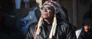 CANNON BALL, ND - DECEMBER 04: Chief Arvol Looking Horse of the Lakota/Dakota/Nakota Nation listens to speakers during an interfaith ceremony at Oceti Sakowin Camp on the edge of the Standing Rock Sioux Reservation on December 4, 2016 outside Cannon Ball, North Dakota. Native Americans and activists from around the country have been gathering at the camp for several months trying to halt the construction of the Dakota Access Pipeline. Today the US Army Corps of Engineers announced that it will not grant an easement for the pipeline to cross under a lake on the Sioux Tribes Standing Rock reservation, ending the months-long standoff. The proposed 1,172-mile-long pipeline would transport oil from the North Dakota Bakken region through South Dakota, Iowa and into Illinois. (Photo by Scott Olson/Getty Images)